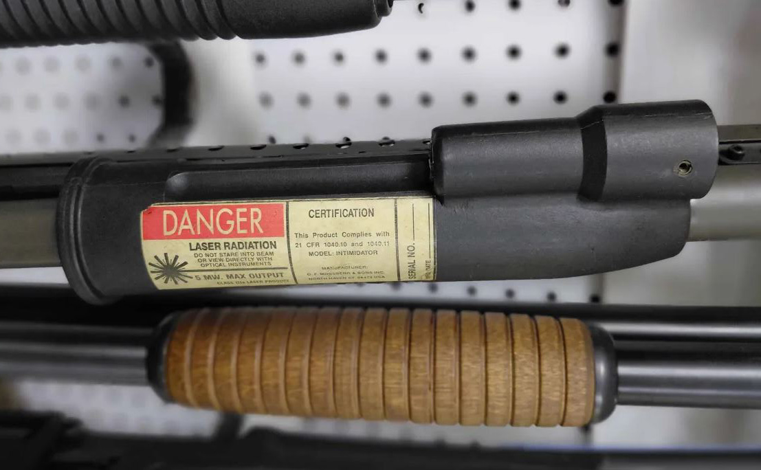 Close-up of a laser device with a warning label indicating 'Danger Laser Radiation' attached to a firearm.