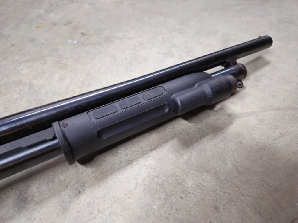 Close-up view of a factory option laser attachment with three buttons, mounted on a shotgun forearm.