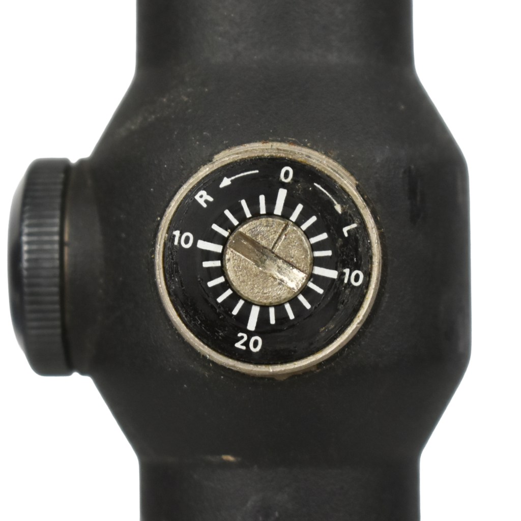 Close-up view of a sight adjustment knob featuring markings for windage and elevation on a black optic device.