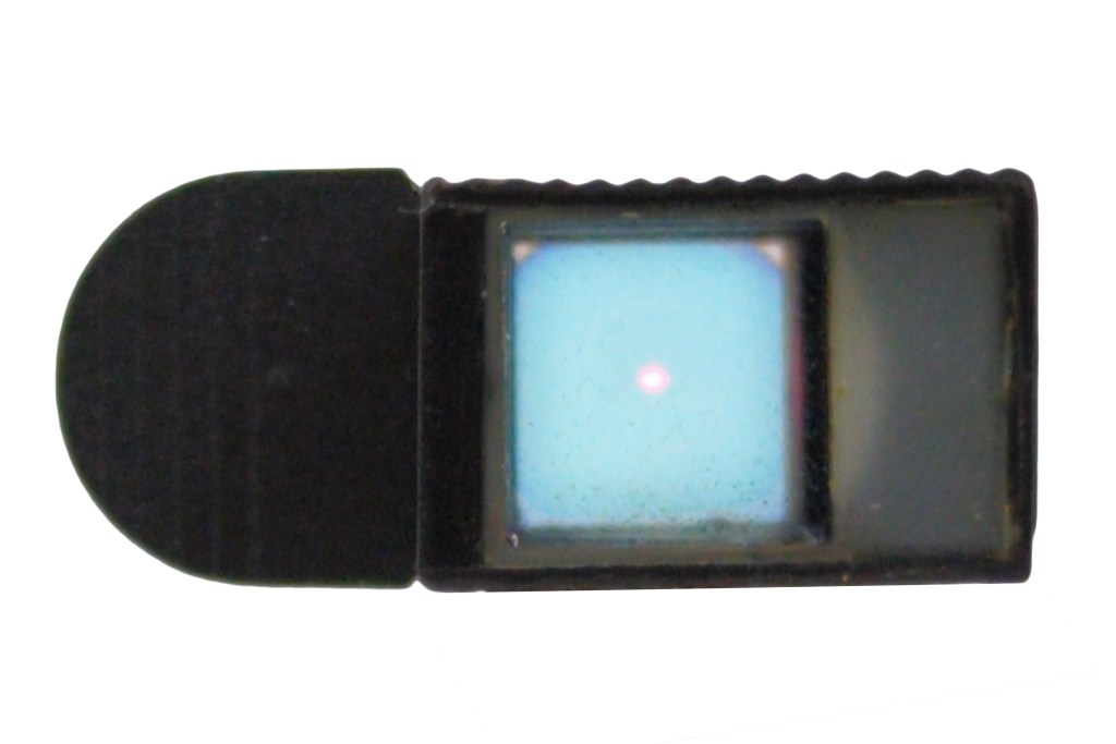 A close-up view of the Electro Prismatic Collimator sight showing its small rectangular shape and the reflection of a red dot in the aiming window.