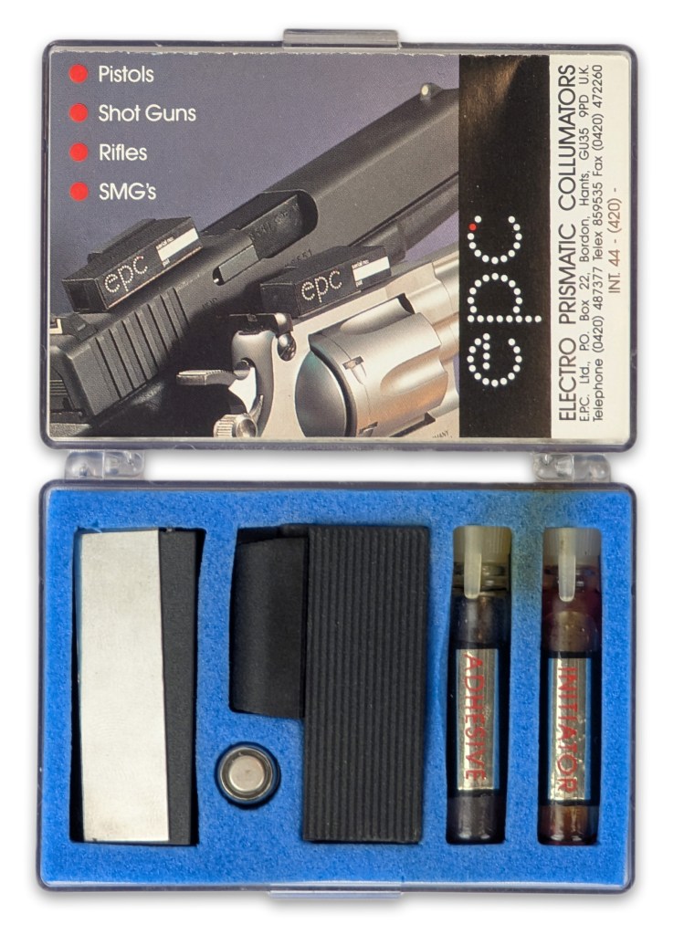 A clear plastic case containing an Electro Prismatic Collimator optic kit, featuring an optic mounted on a firearm, along with two vials labeled 'ADHESIVE' and 'INITIATOR', a mounting tool, and additional components.