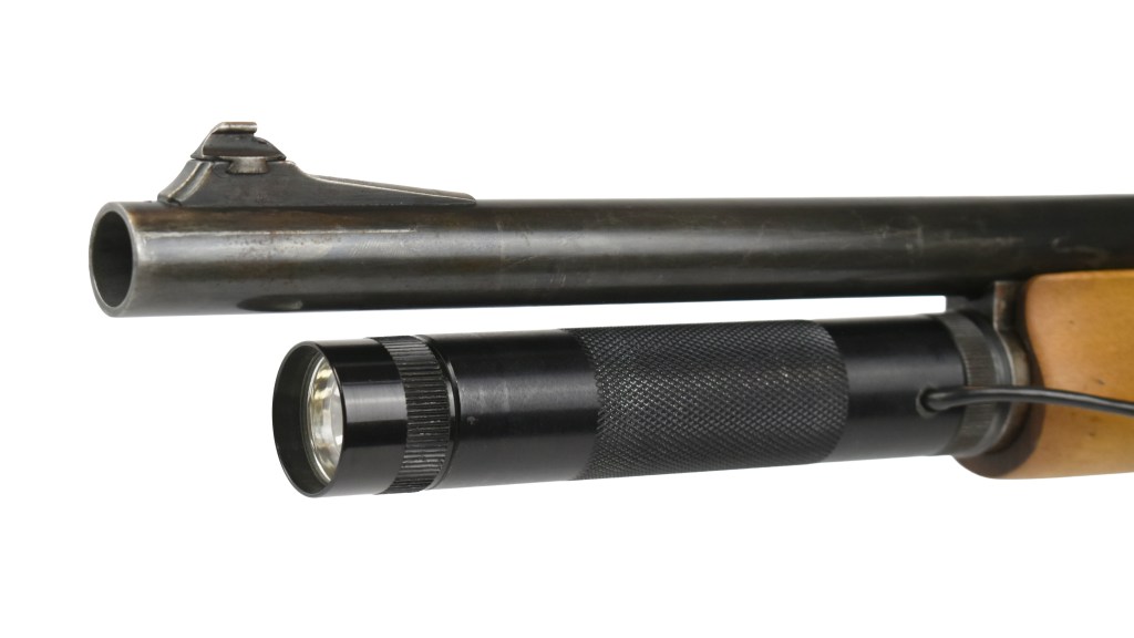 Close-up view of a shotgun with a mounted flashlight, showcasing the barrel and light attachment.